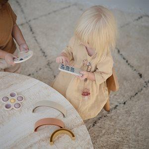 Blondwłosa dziewczynka bawi się telefonem z silikonowymi przyciskami, marki Mushie.
