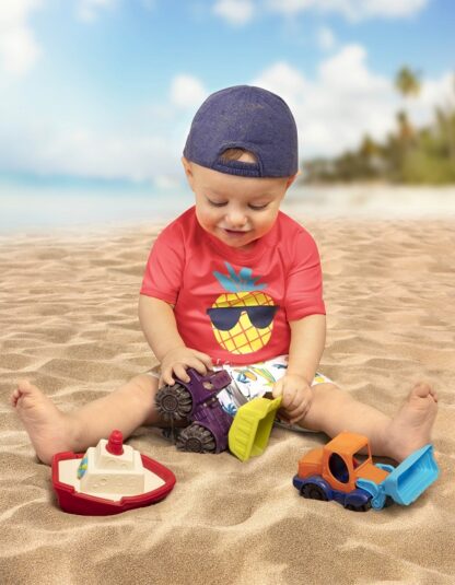 Chłopiec bawi się trzema pojazdami, marki B.toys na plaży.